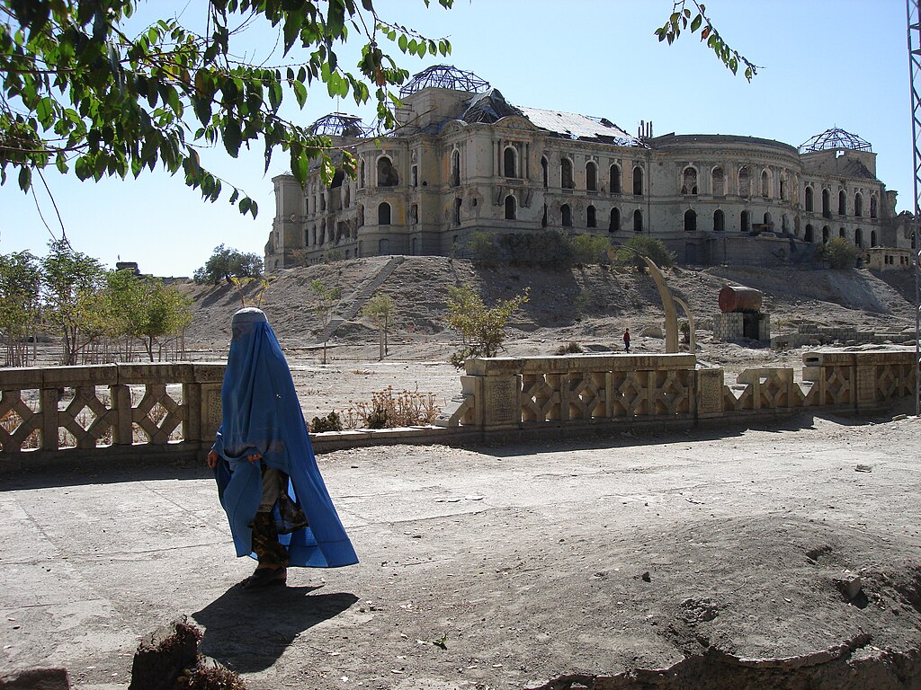 A woman in a blue burqa walks past a ruined building