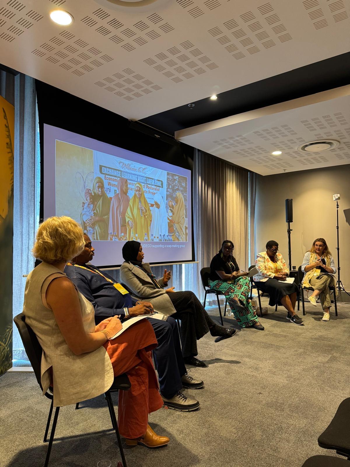 A group of people are seated on a stage talking with a screen behind them