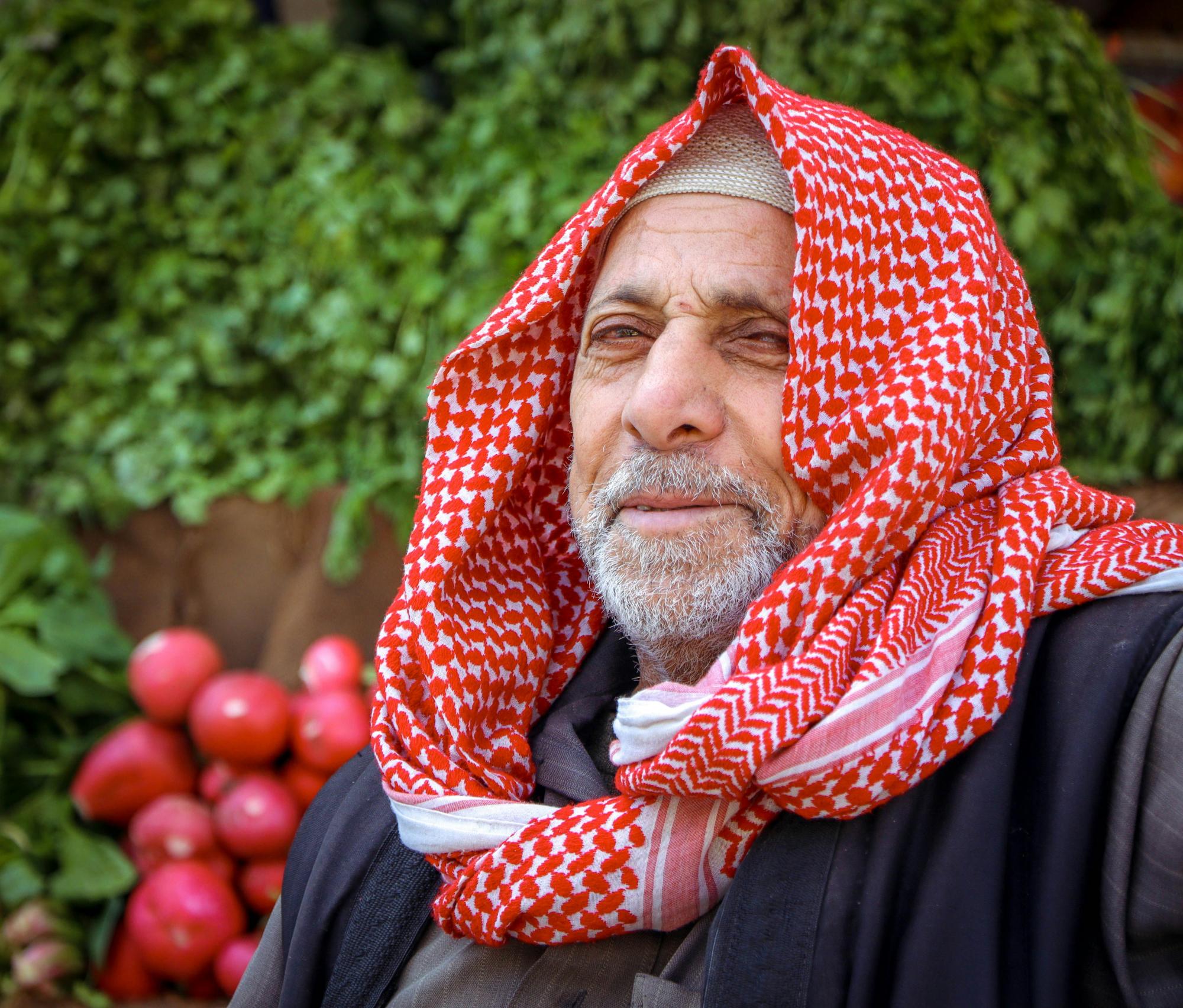 A man in a red and white keffiyeh / scarf looks at the camera