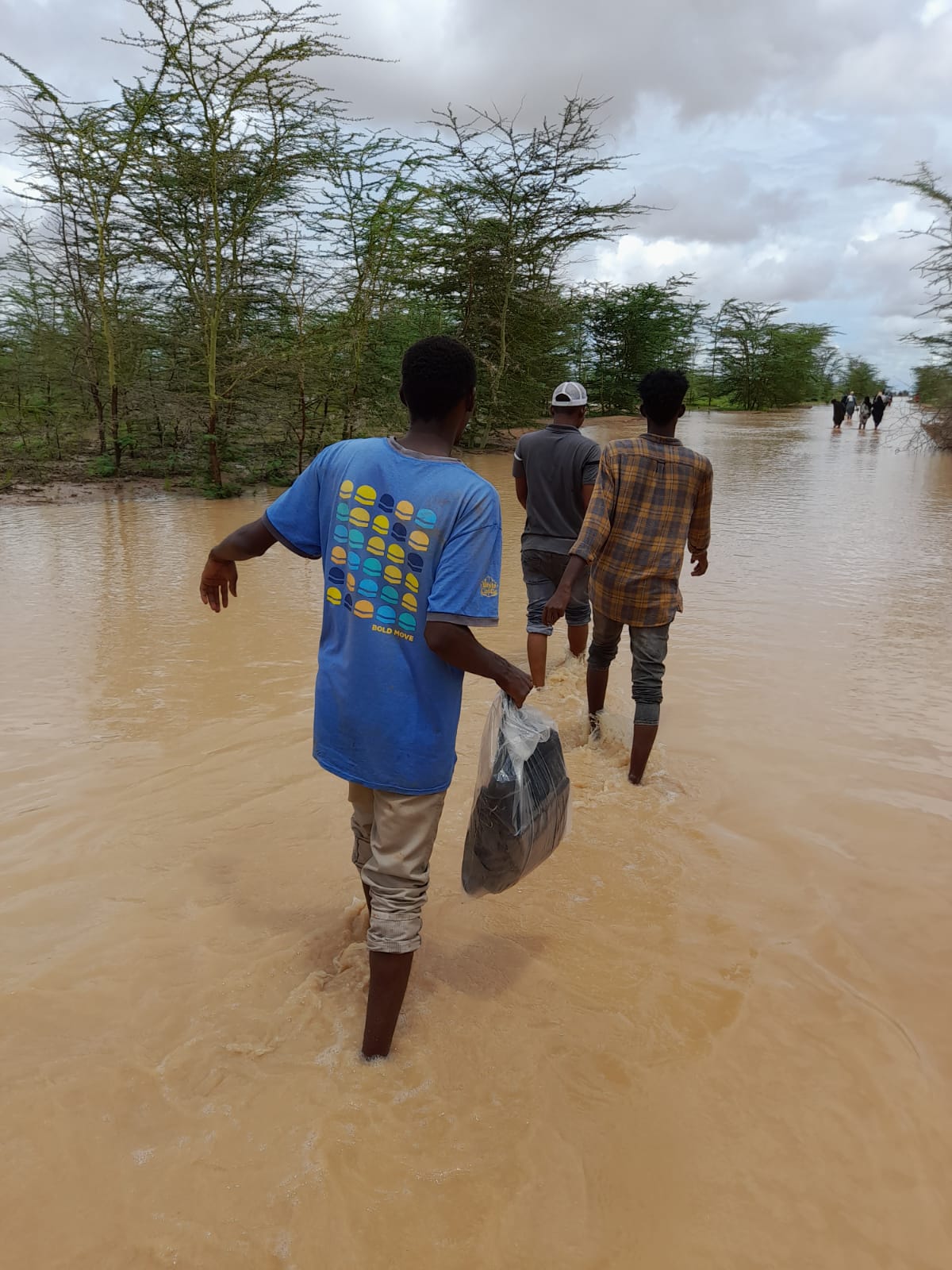 A group of men walk away from the camera as they wade through flood water