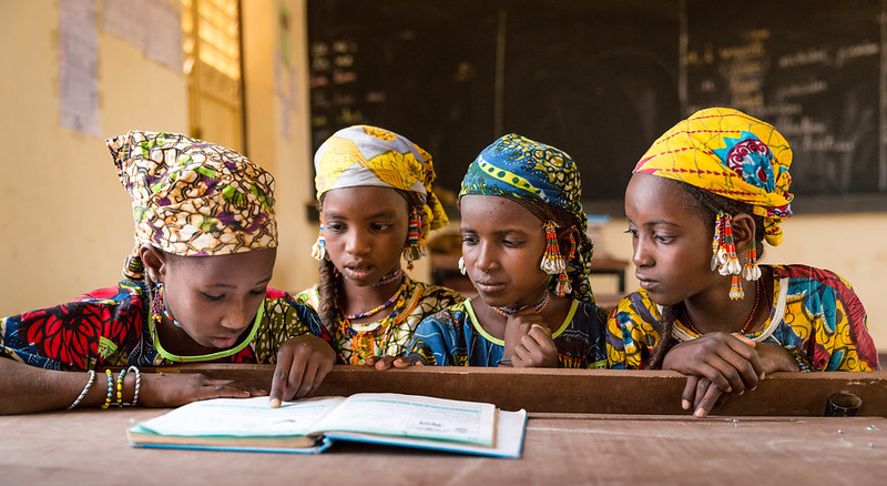 Four young girls sit together at a desk looking at a textbook