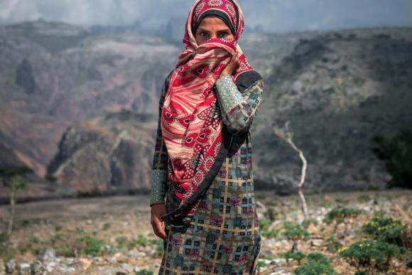 Close up of a young woman standing with her face covered looking at the camera