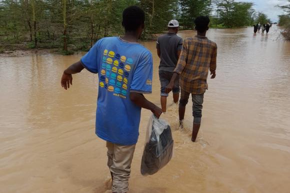 A group of men walk away from the camera as they wade through flood water