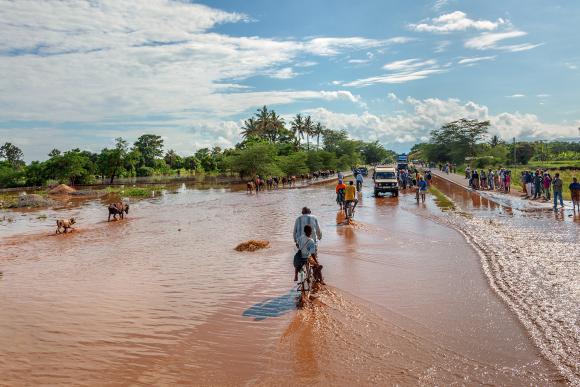 A man on a bicycle rides through flood murky waters into the distance