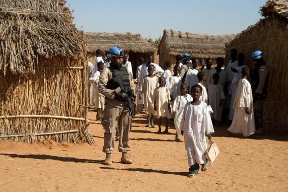 A UN soldier with a gun patrols a camp as children walk by