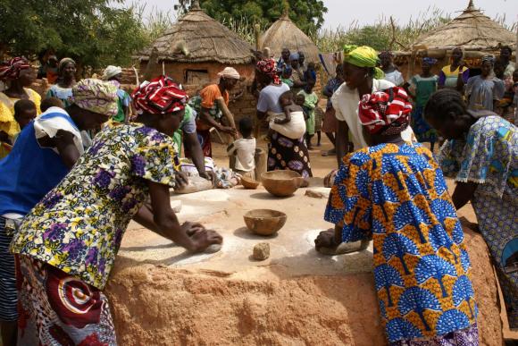 A group of women stand in a circle kneading millet