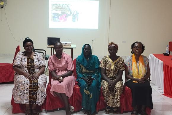 Five women sit in a line in a room and look at the camera