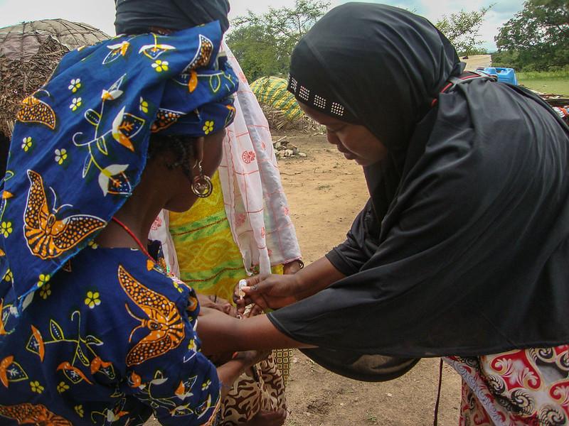 A woman vaccinating a small child who is being held by the mother