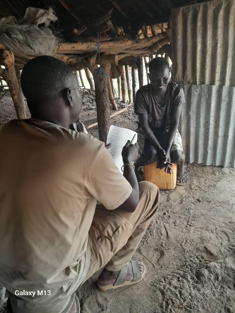 A pastoralist sits in the background facing the camera while being interviewed