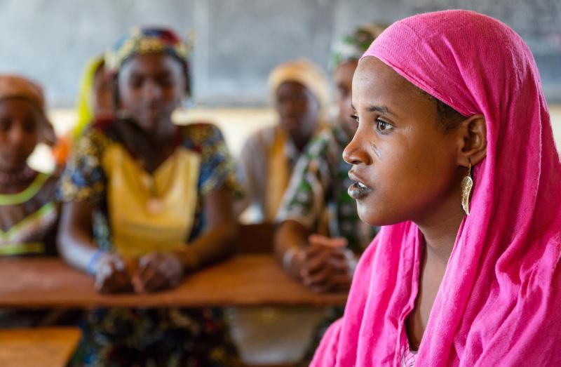 A young woman sits in profile speaking to students in a classroom
