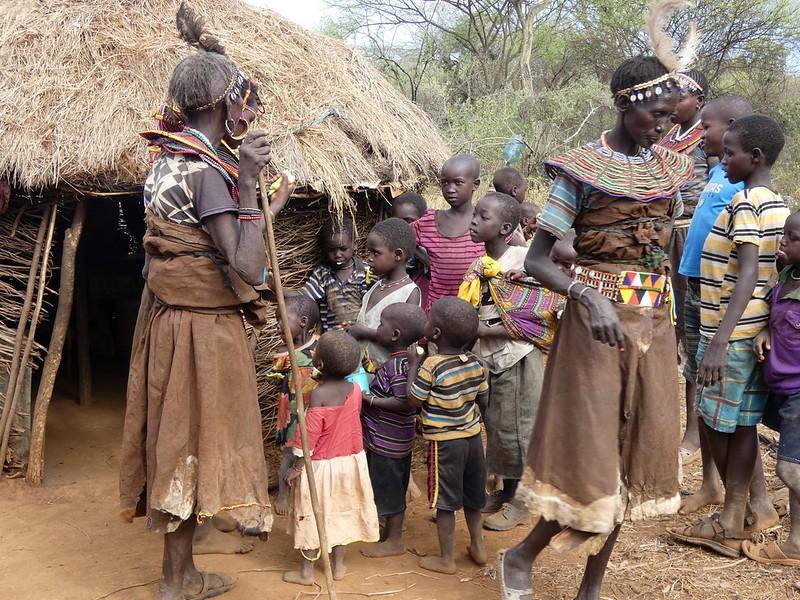 Women and children stand outside a thatched hut