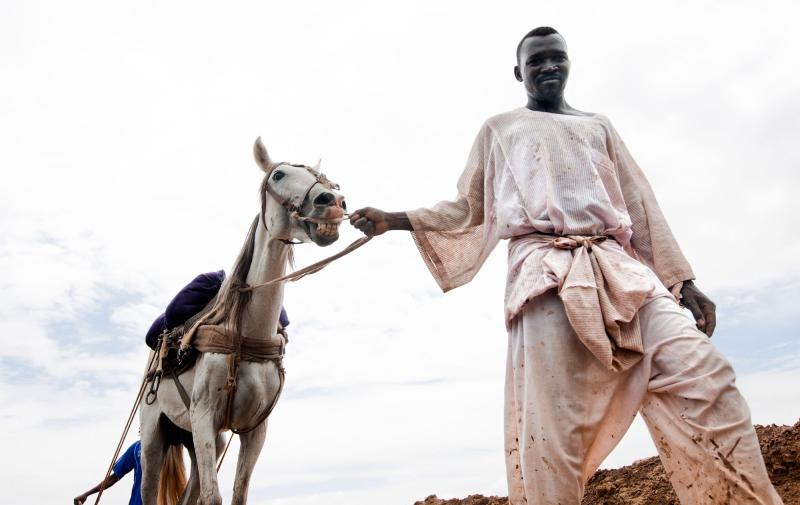 A man walks through a muddy field leading a horse