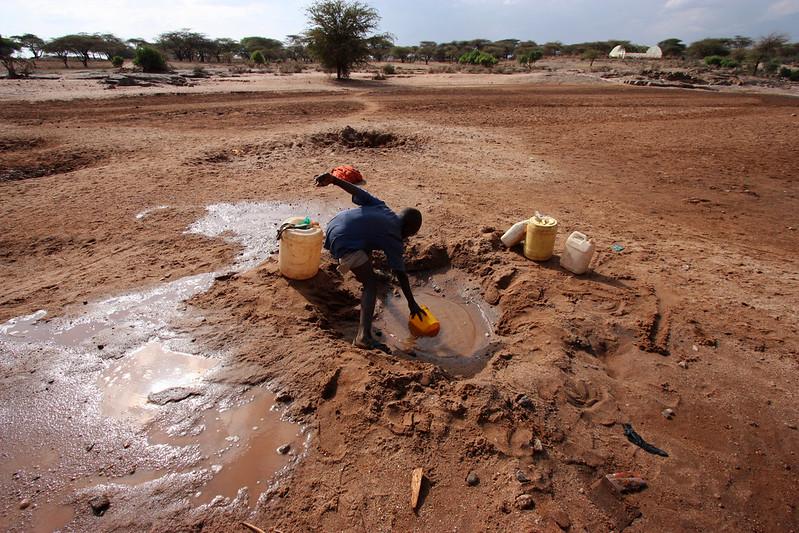 Man stands above shallow water source in drylands, scooping out water with buckets