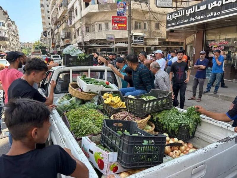 A group of men stand in a road near the back of a parked pickup trick filled with crates of vegetables and fruit