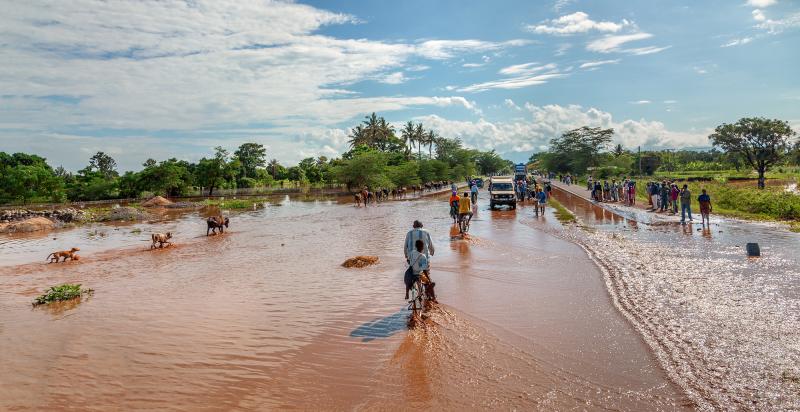 A man on a bicycle rides through flood murky waters into the distance