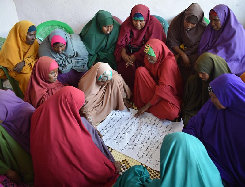  A group of women sit on the floor together indoors looking at posters
