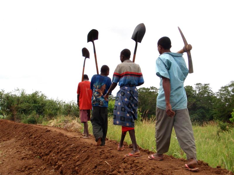 Four men walk along an embankment carrying tools
