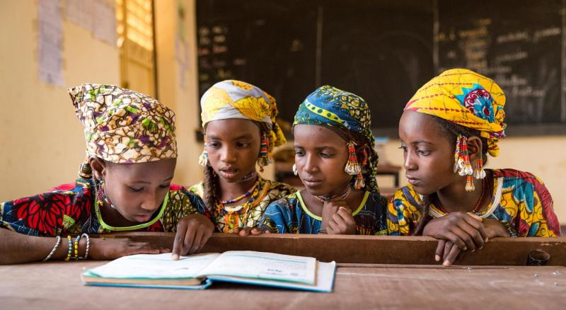 Four young girls sit together at a desk looking at a textbook