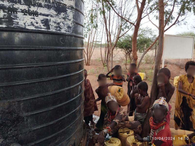 Women and children fill cans from a leaking water system.