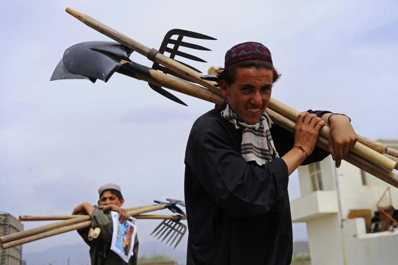 Two men walking outside carrying farm tools over their shoulders