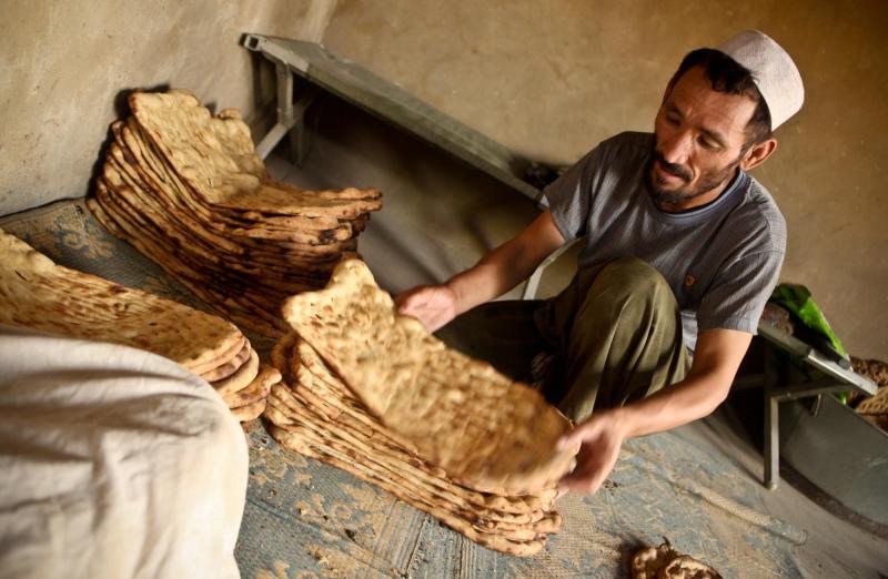 Man crouches on the ground inside, arranging stacks of fresh bread