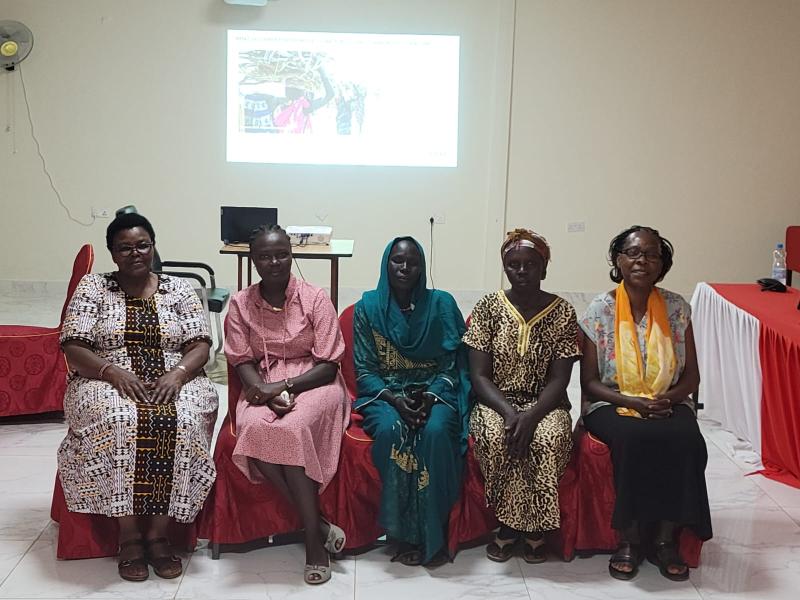 Five women sit in a line in a room and look at the camera