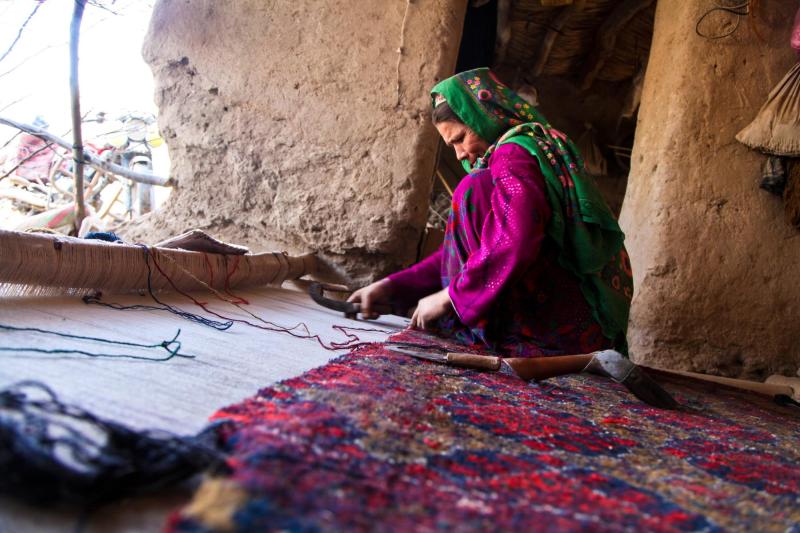 A woman crouches inside a room as she weaves a carpet by hand