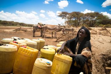A woman fills plastic containers with water and ties them to a donkey
