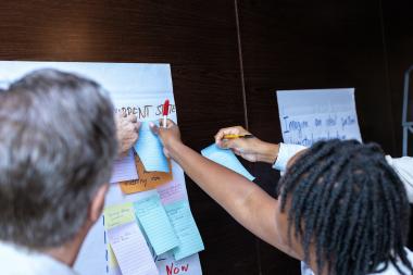 Two people write on post it notes that are pasted on to a flip chart