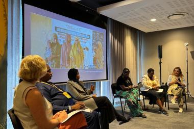 A group of people are seated on a stage talking with a screen behind them