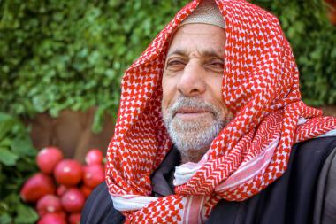 Close up of a man wearing a red and white keffiyeh/ headscarf with vegetables in the background