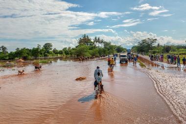 A man on a bicycle rides through flood murky waters into the distance