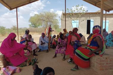 A group of women gather under a shelter on a sunny day