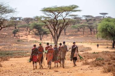 Eight women walking on a winding red dirt path with trees in the background