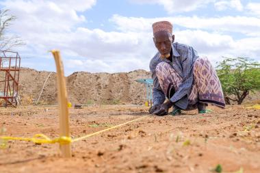 A man crouches down as he measures a plot of farmland